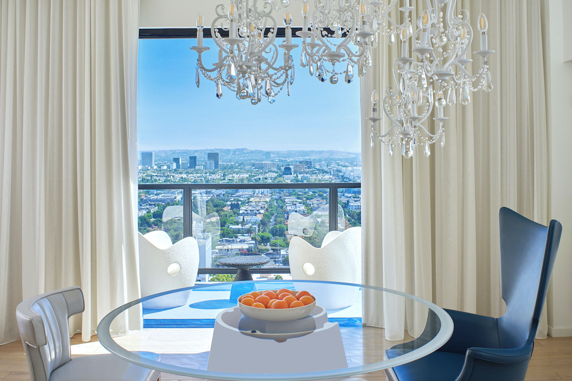 Table with bowl of fruit and chair and balcony with view of Los Angeles.