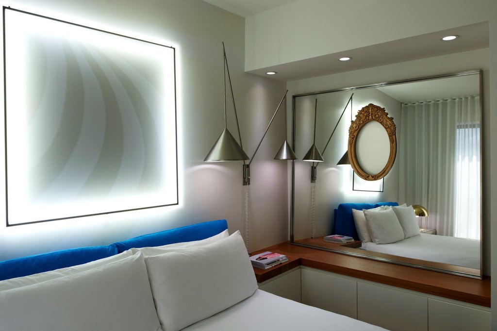 A cozy bedroom with a neatly made bed and a sleek mirror on the wall.