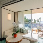 Cream lounge sofa with round coffee table in front of it and beach scene in the windows behind it