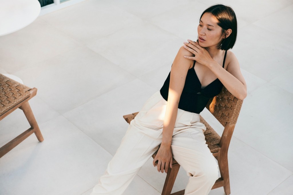 a striking woman sitting in a woven chair with sunlight peeping through shadows over her arm