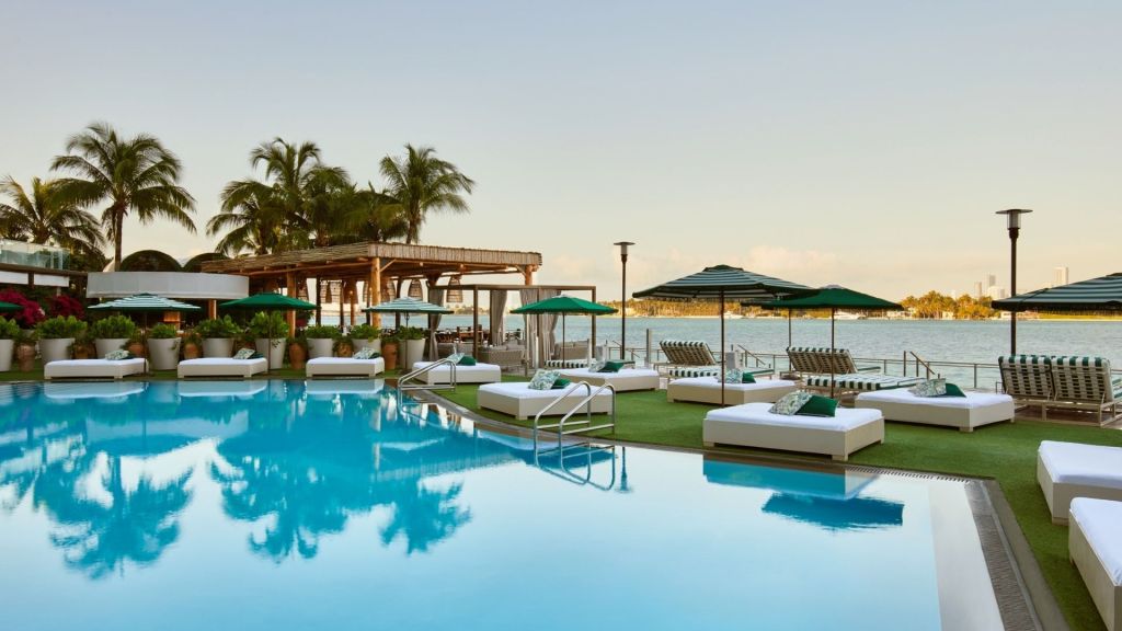 Pool deck with white loungers, cabanas, and palm trees