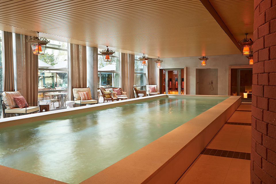 Long indoor pool captured from the side with lounge chairs positioned on one side by windows