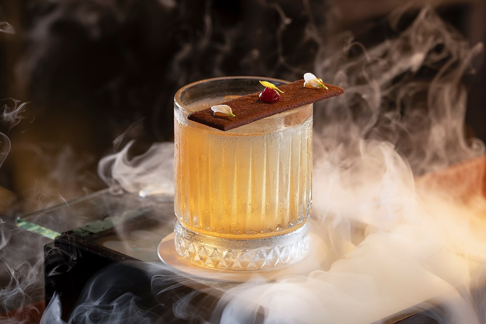 Yellow cocktail with a garnish and smoke surrounding it