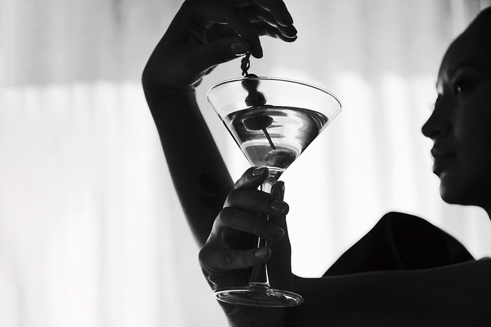 Black and white, close up photo of a woman holding a martini glass with three olives.