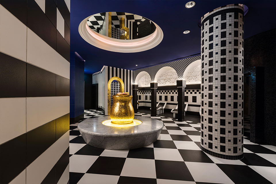 Mondrian Doha spa with black and white checkered floors, a blue ceiling with a mirror, and a large, gold and marble seating area.