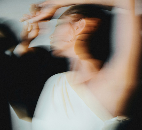 Blurry image depicting a woman in a white one shoulder dress dancing in motion.