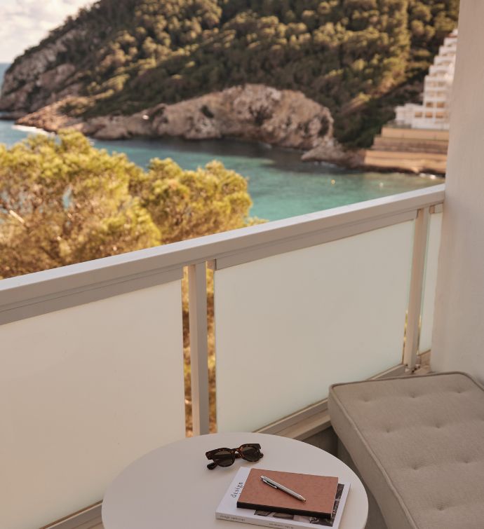 Outdoor balcony with cream bench, small white table, and view of the sea with green mountains