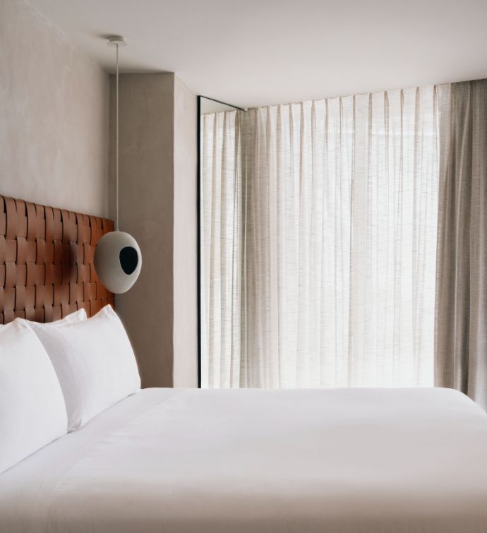 Side of white bed with rust colored headboard and curtains covering a balcony window