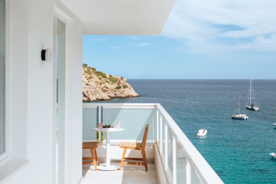 Large white balcony with table and chairs looking out to a blue sea with boats