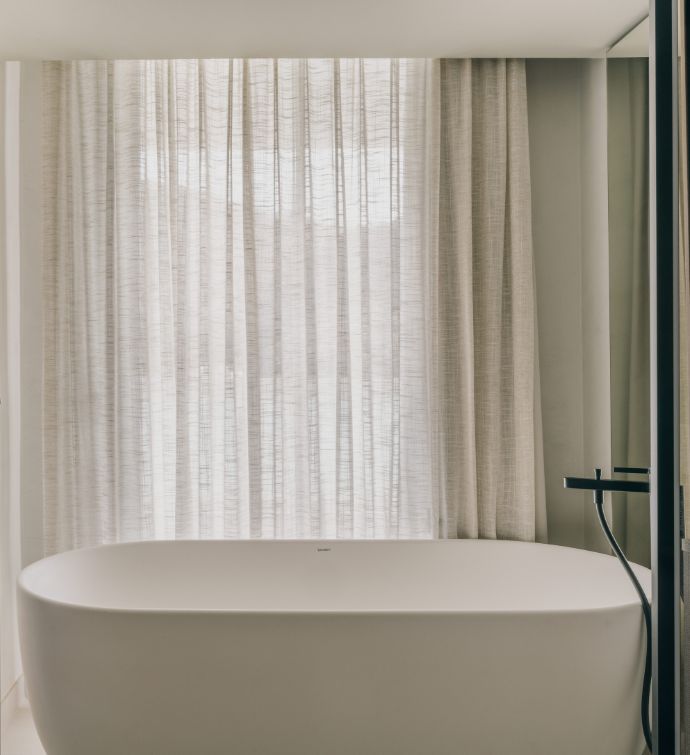 Large white bathtub with white curtains covering big windows