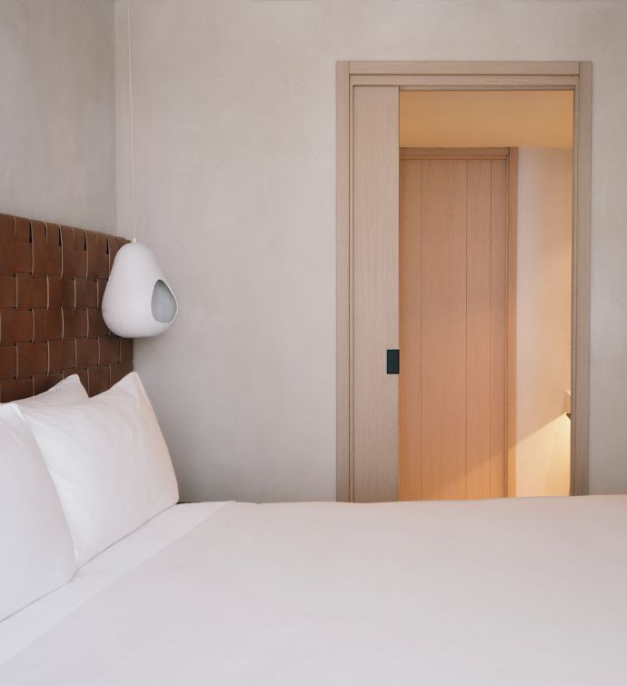 White bed with rust colored headboard and a door to another room in the background