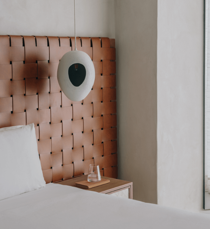 A neatly made bed with white sheets and a lamp hanging above the bedside table