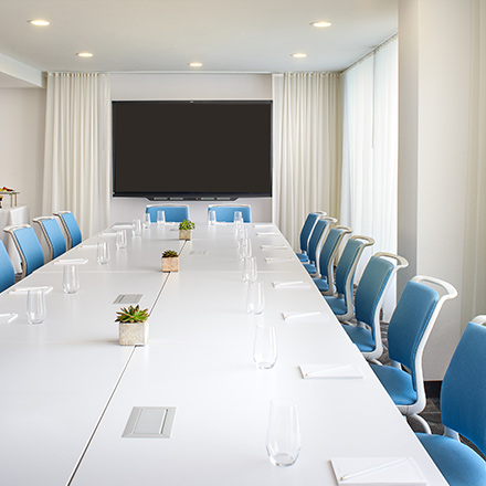 Large, white boardroom with a long table, blue chairs and TV.