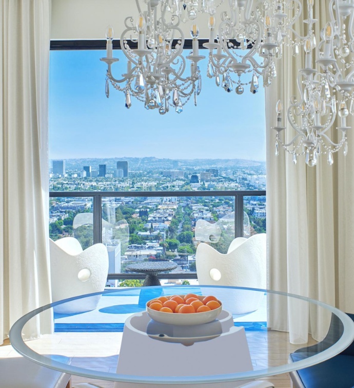 Clear table with a bowl of oranges, a chandelier over it and a view of Los Angeles