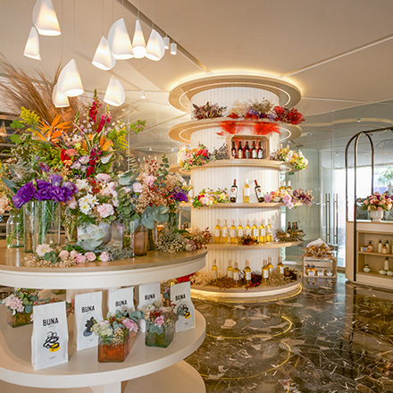 Bright gift shop with round shelves filled with different colored flowers in vases and wine bottles on shelves in the background.