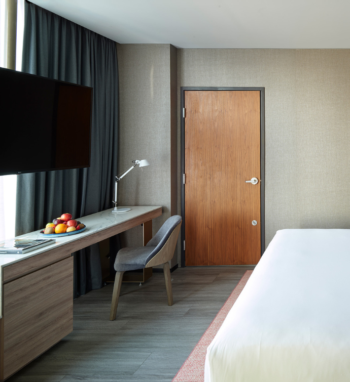 a desk in a hotel room with natural light and a mounted HDTV
