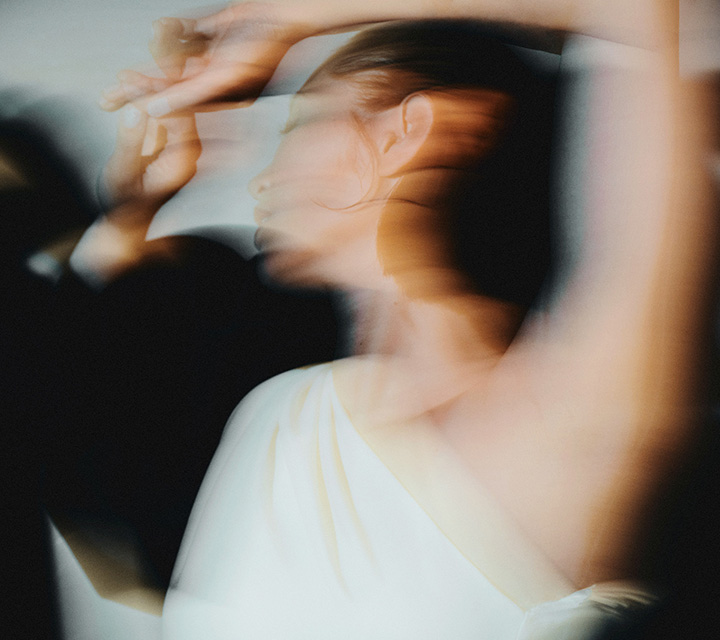 Blurry image depicting a woman in a white one shoulder dress dancing in motion.