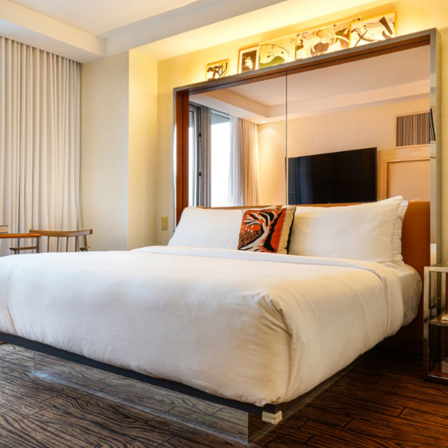 Large white bed with mirrored headboard and orange patterned throw pillow in a hotel room