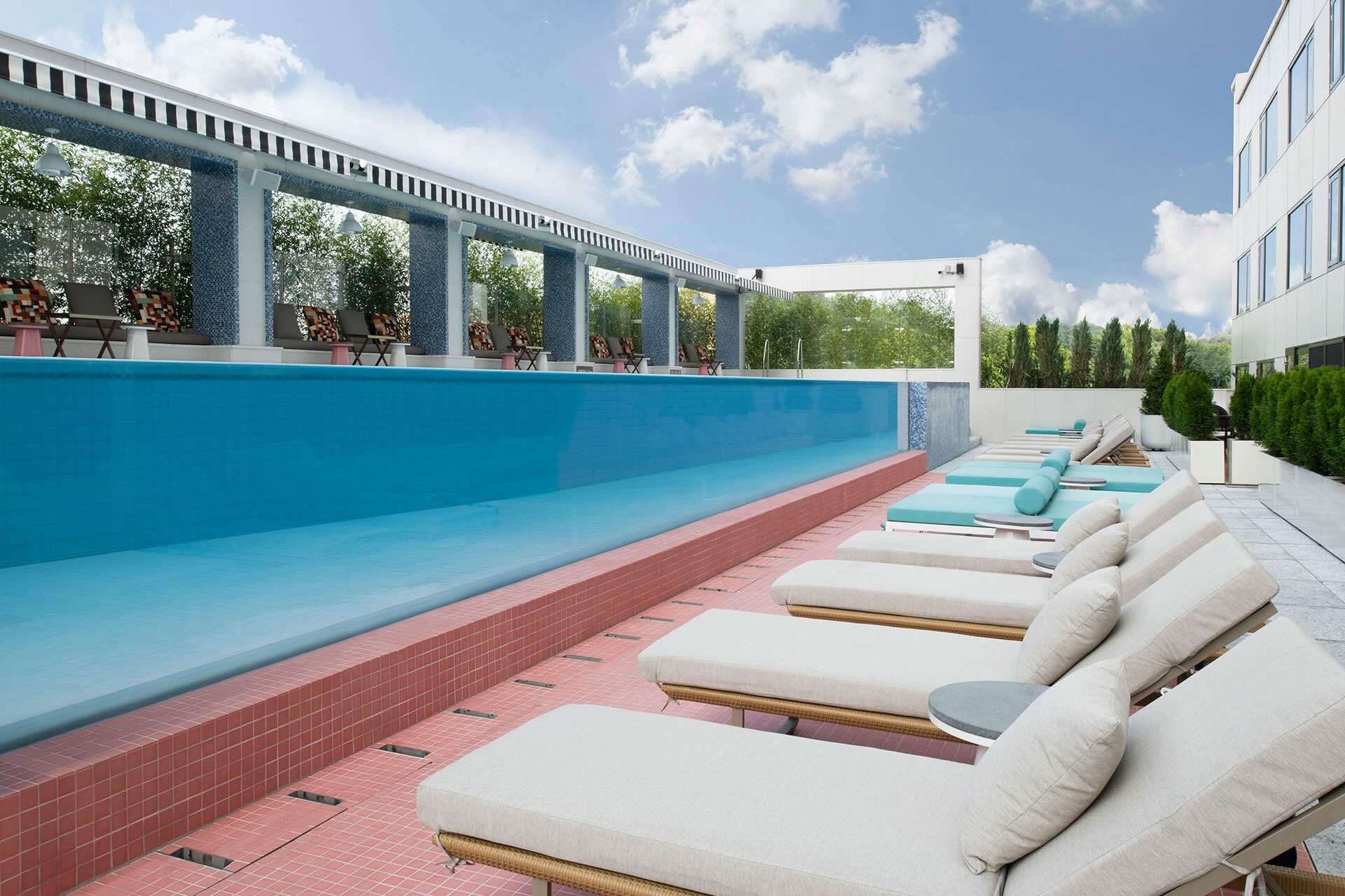 Side of infinity pool, red-tiled pool deck, and row of cream and turquoise chaise lounges