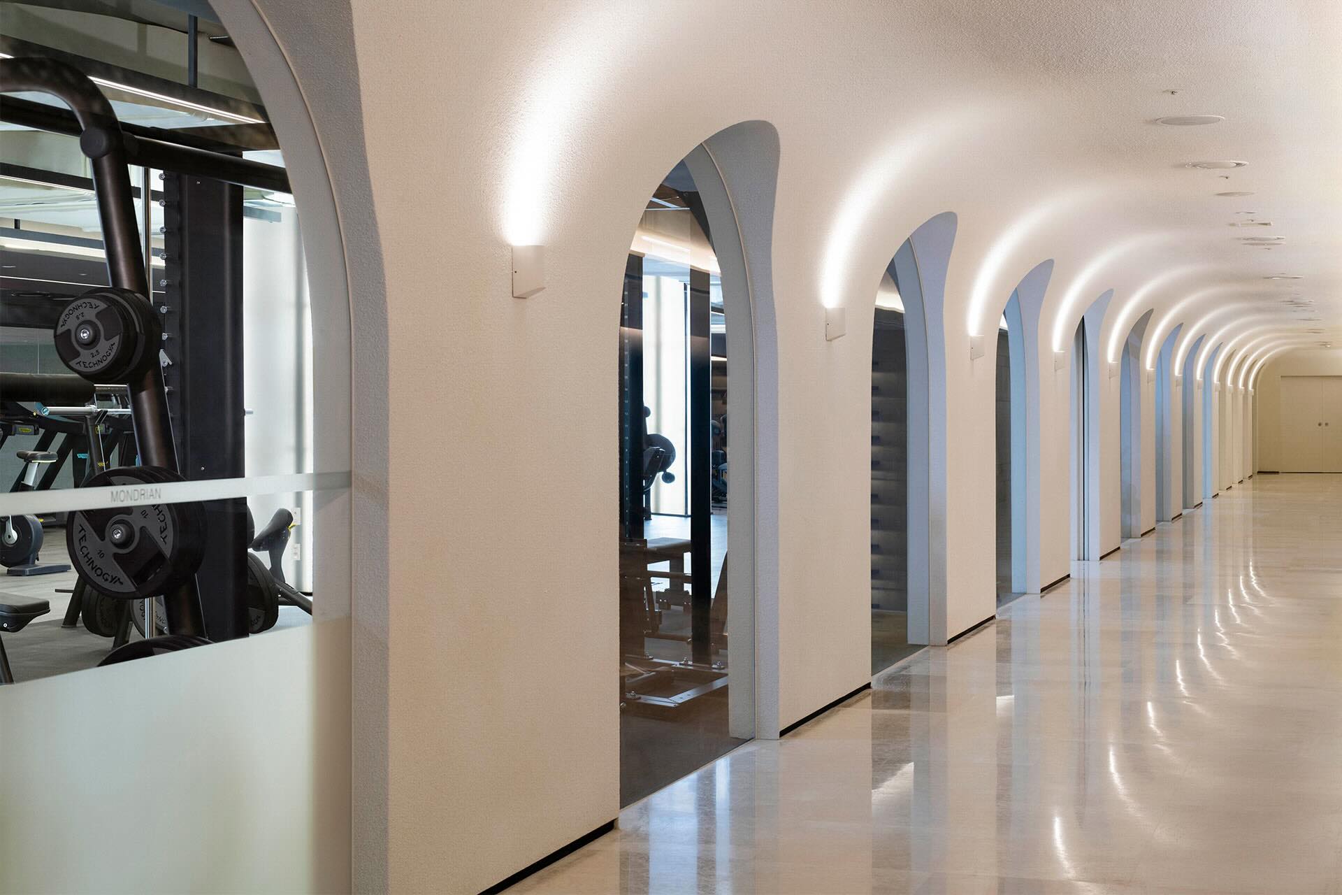 Large white hallway with arched entrances looking into a gym full of equipment