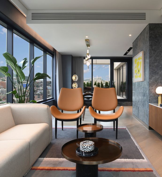 Two light brown modern chairs on a patterned rug with dark brown coffee table and white sofa in the corner