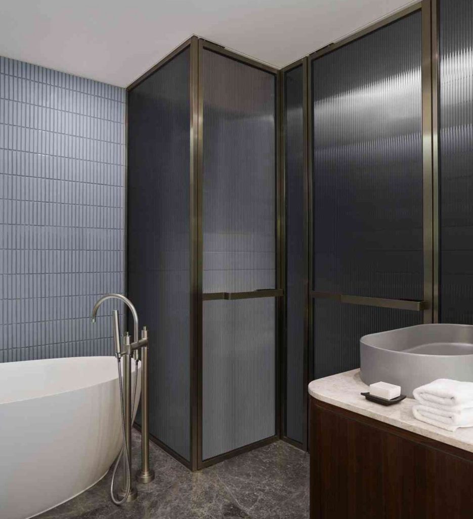 Blue tiled bathroom with walk-in shower, free-standing white bathtub, and corner of a marble counter with grey sink