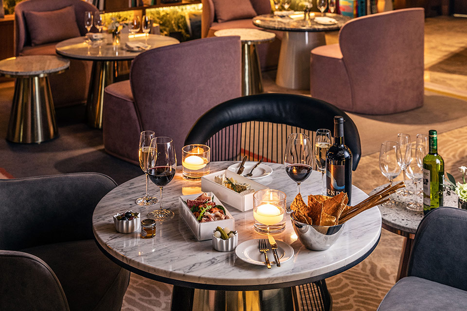 Round marble dining table with glasses of red wine, bread basket, and candles on the table, purple lounge chairs surround the table. 