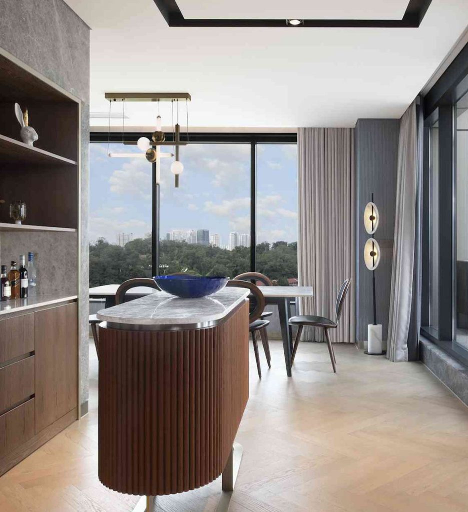 Modern kitchenette with wooden island, counter with bottles of liquor, and a large rectangular table with chairs in the distance