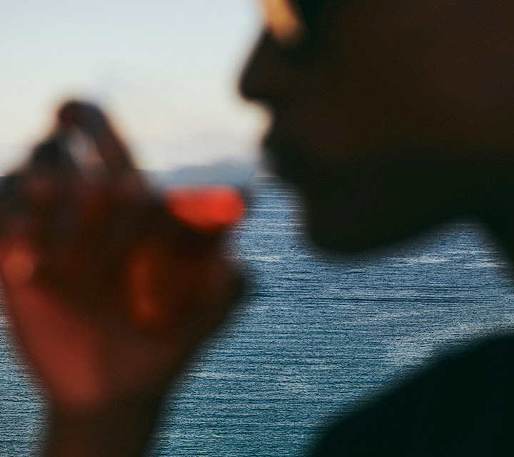 Blurry image of a man drinking a cocktail, with the ocean in the background in focus.