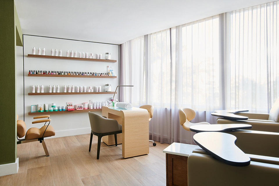 A nail salon with natural light featuring chairs and shelves with beauty products on the wall.