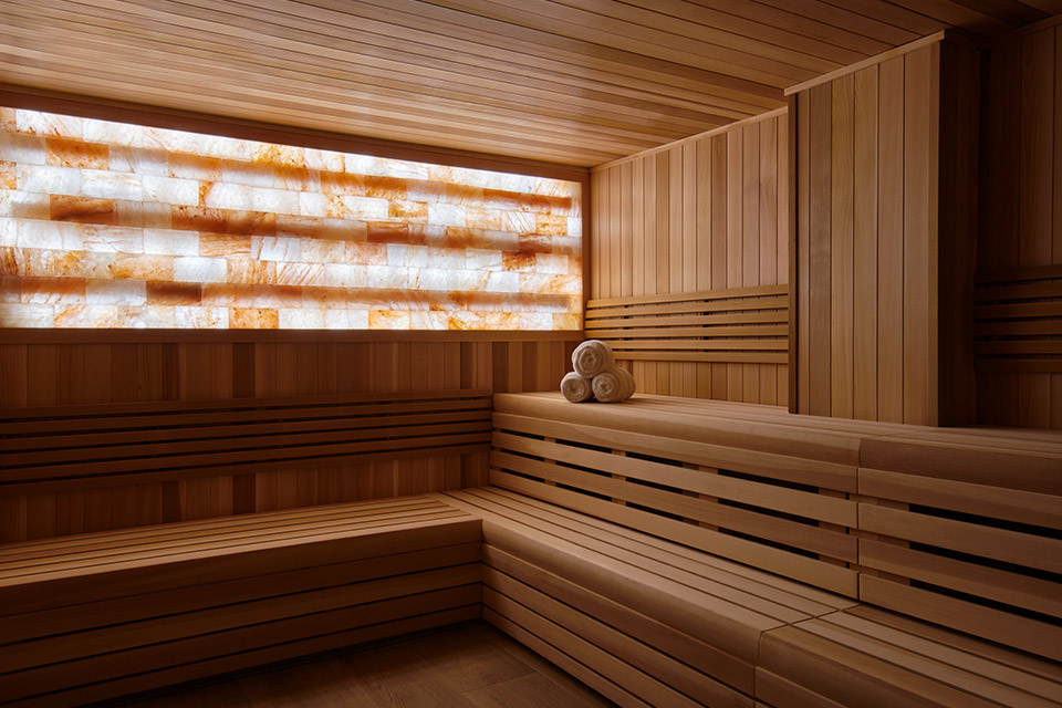 A relaxing wooden sauna with salt stones on the wall and rolled spa towels.