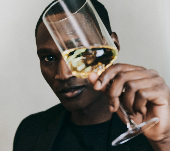 Man holding a glass of white wine over his face.