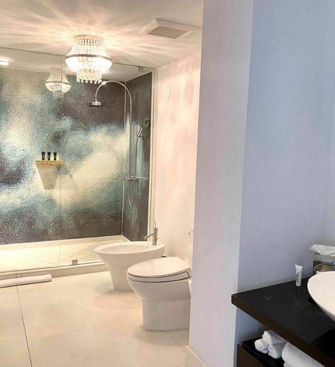 Two toilets and walk-in shower in a bathroom with one blue colored wall and a small crystal chandelier hanging from the ceiling