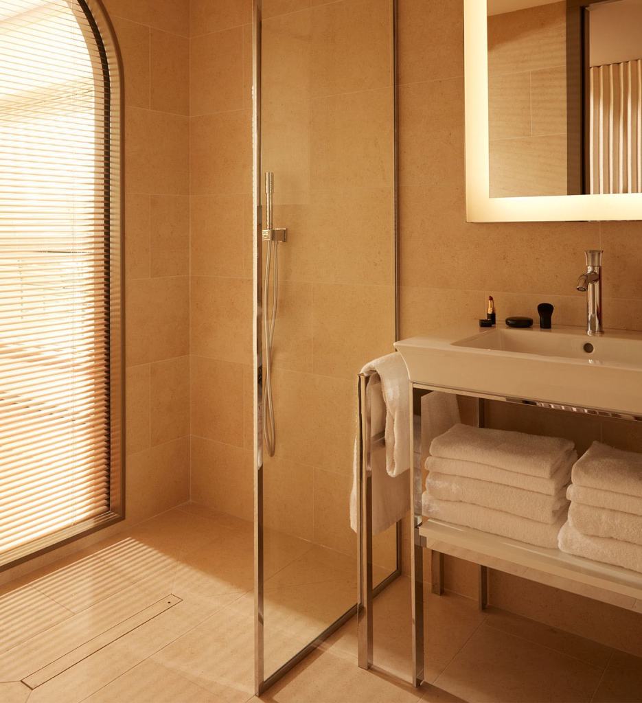 Bathroom with an illuminated mirror, shower and sink with towels beneath it