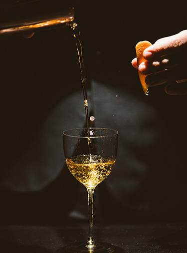 Champagne-colored cocktail being poured from above, and about to be garnished with an orange peel