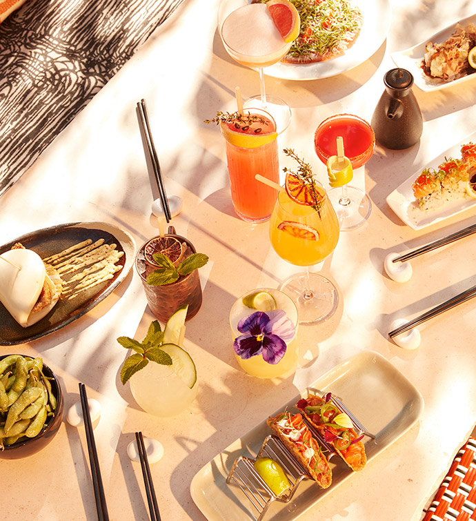 Variety of dishes and cocktails captured from overhead, in the sunshine