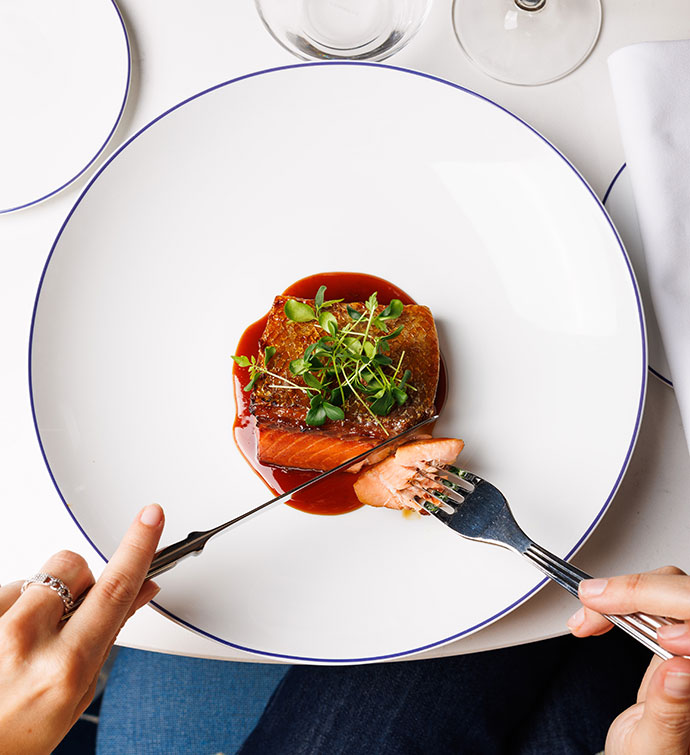 A pair of hands cutting into a filet of fish with a fork and knife