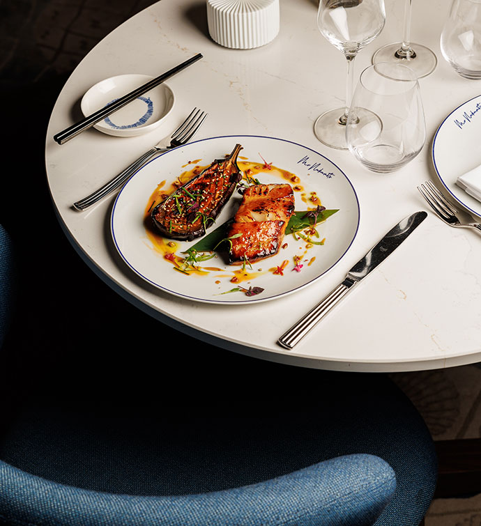 A plate of black cod from Mr Nakamoto Cannes, on a set dining table in front of a blue chair