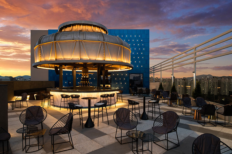 Outdoor lounge space with small black outdoor chairs and bistro tables with a circular, modern bar with domed roof in the background.