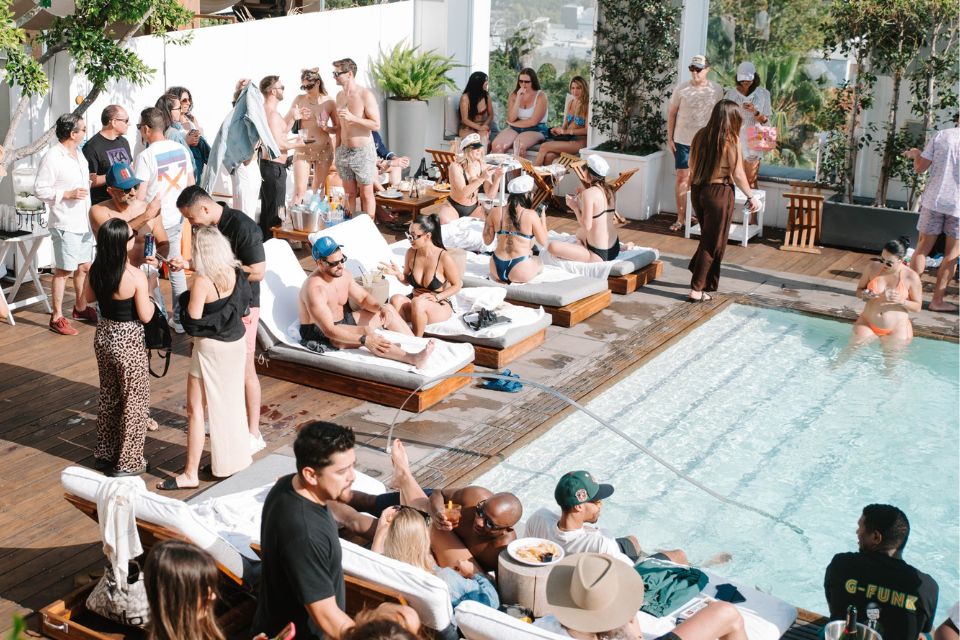 Outdoor pool with daybeds and lots of people sitting and standing around the pool