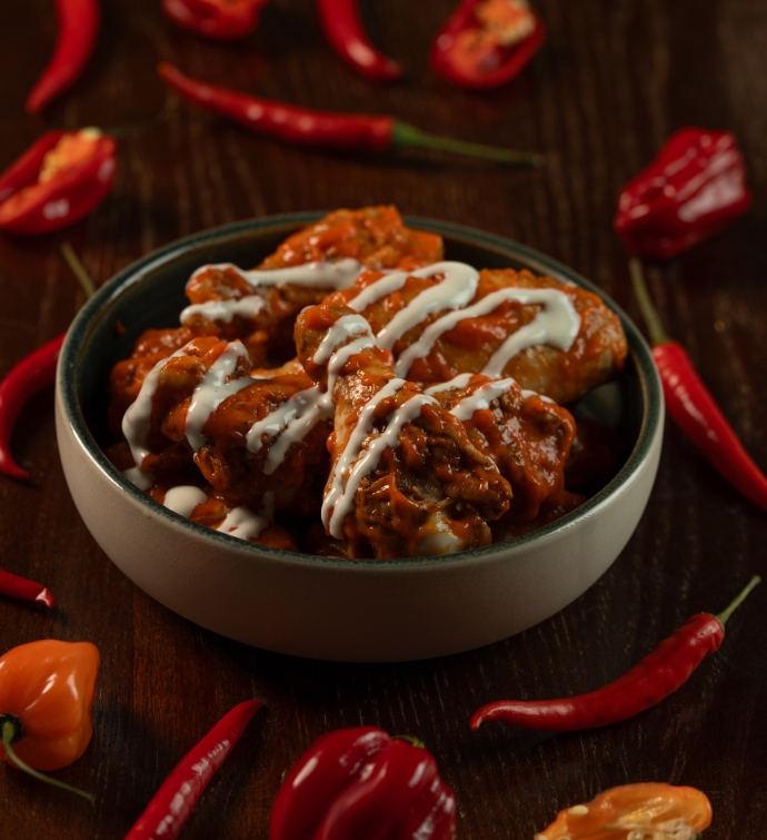 Bowl of chicken wings with sauce surrounded by chili peppers at Hudson Tavern Doha