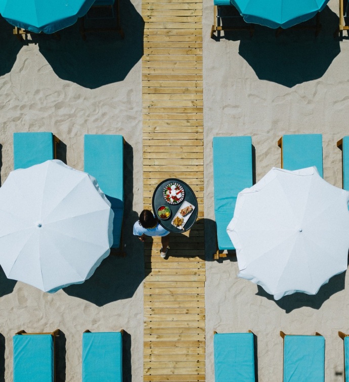 aerial photo of a server walking down the beach with teal daybeds and white umbrellas