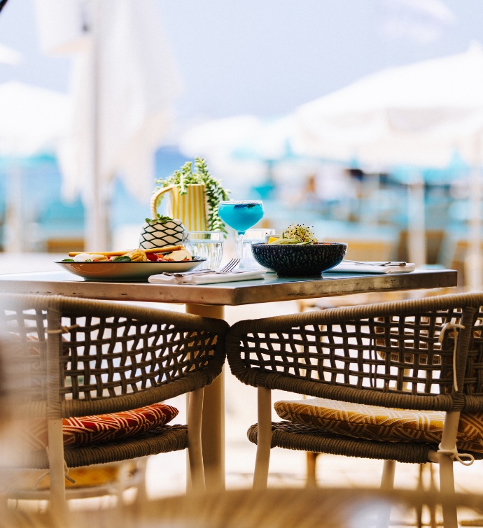 al fresco dining table with cocktails and plates of food and umbrellas in the background