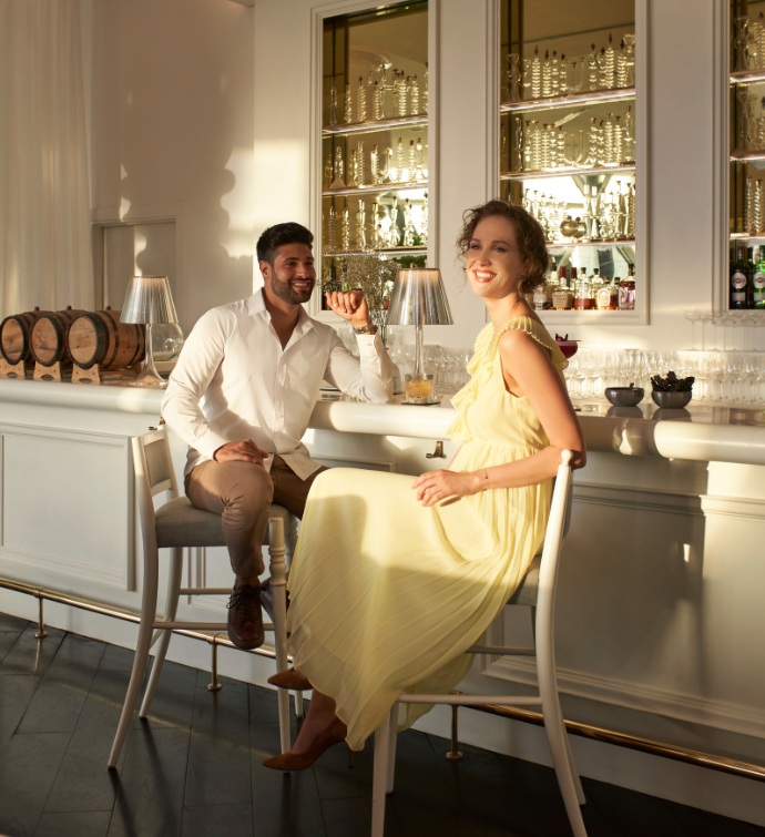 A woman in a yellow dress and man in white shirt and khakis sitting at a bar