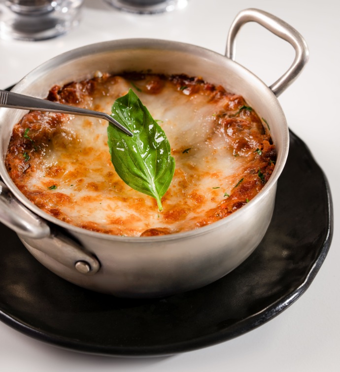 Placing a basil leaf on top of a dish consisting of red sauce and cheese in a silver skillet