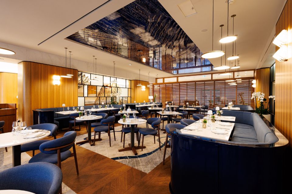 Large dining room with warm wood walls, navy banquette seating, white tables, and navy upholstered dining seats