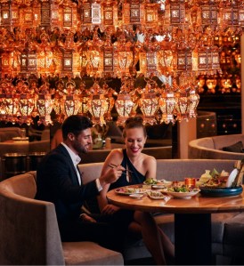 A giant chandelier made of lanterns over a couple enjoying sushi at Morimoto Doha