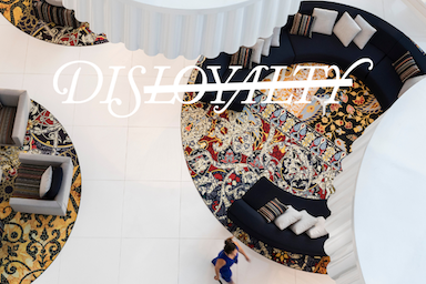 Aerial view of a lobby with white tile floors, decorative rugs, and black curved sofas with text in white that says 'DISLOYALTY'