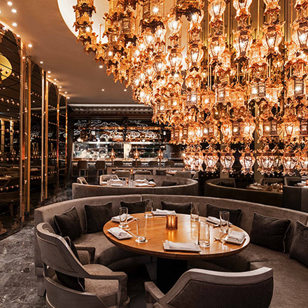 Restaurant with round seating with comfy chairs, and an oversized chandelier in the middle of the room at Morimoto Doha.