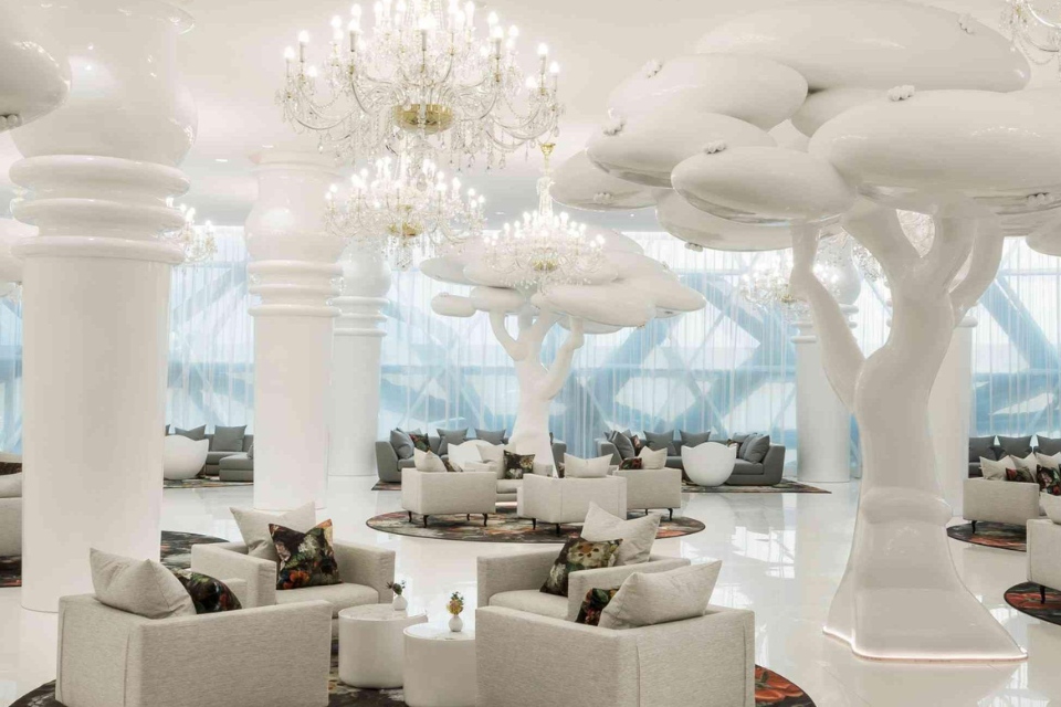 Large, white hotel lobby with oversized white trees, chandeliers and seating